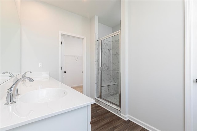 full bathroom with a spacious closet, baseboards, a stall shower, double vanity, and wood finished floors