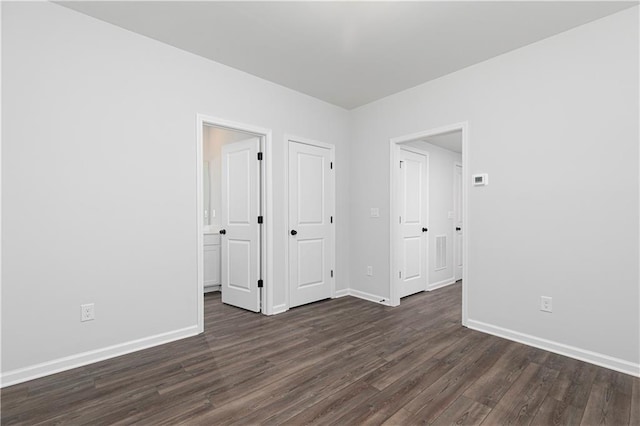 unfurnished bedroom with ensuite bathroom, dark wood-style floors, and baseboards