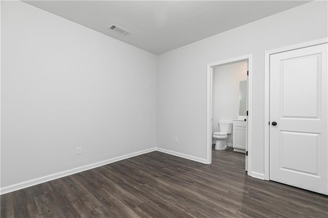 unfurnished bedroom with connected bathroom, baseboards, visible vents, and dark wood-style flooring