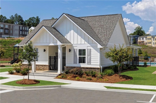 view of front of house featuring board and batten siding, a front yard, a shingled roof, and fence