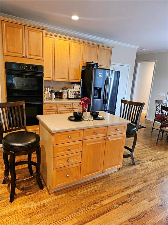 kitchen featuring a kitchen island, double oven, stainless steel fridge, a kitchen bar, and ornamental molding