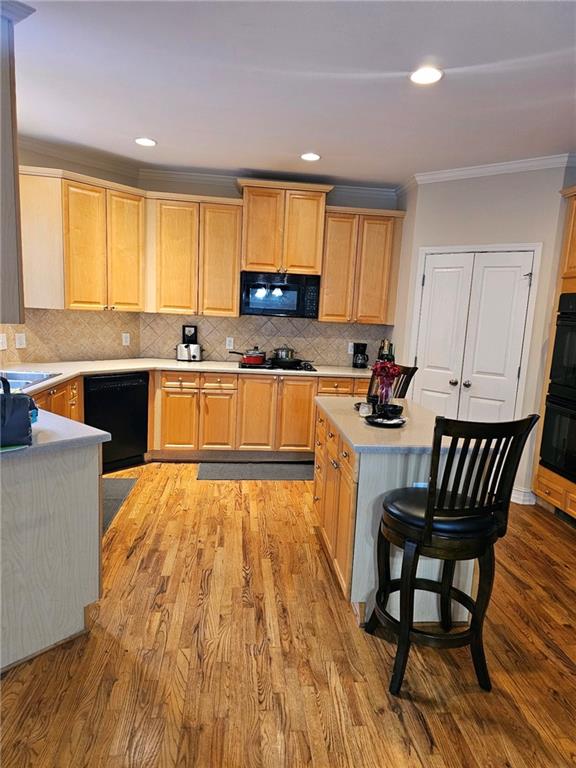 kitchen with tasteful backsplash, ornamental molding, black appliances, light hardwood / wood-style floors, and light brown cabinets