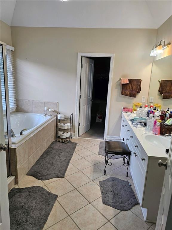 bathroom with lofted ceiling, vanity, a relaxing tiled tub, and tile patterned floors