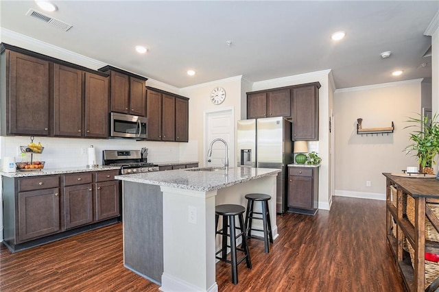 kitchen with light stone counters, stainless steel appliances, dark hardwood / wood-style floors, and a kitchen island with sink