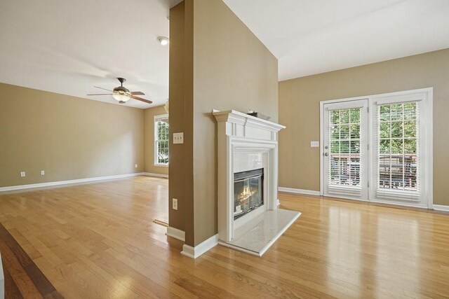 living area with light wood finished floors, baseboards, a ceiling fan, a glass covered fireplace, and stairs