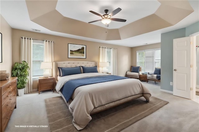 bedroom featuring light carpet, baseboards, visible vents, a raised ceiling, and a ceiling fan