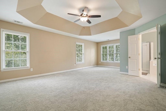 spare room with a tray ceiling, visible vents, light carpet, ceiling fan, and baseboards