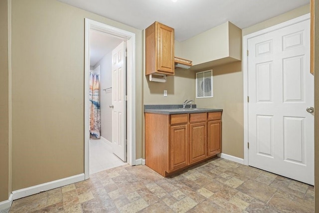 kitchen with stone finish flooring, brown cabinets, a sink, and baseboards