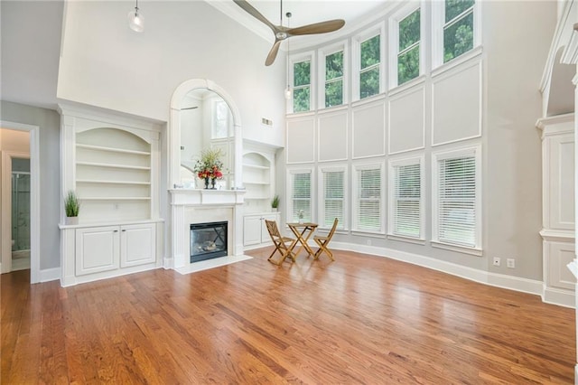 5635 Upper Creek Ct, Suwanee, GA 30024 - unfurnished living room featuring a fireplace with flush hearth, a towering ceiling, ceiling fan, built in shelves, and wood finished floors