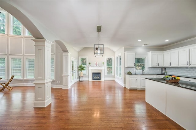 5635 Upper Creek Ct, Suwanee, GA 30024 - kitchen featuring decorative columns, hardwood / wood-style flooring, dark countertops, open floor plan, and vaulted ceiling