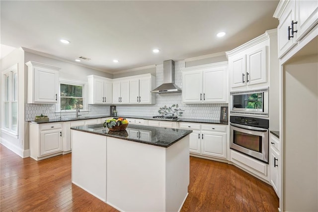 5635 Upper Creek Ct, Suwanee, GA 30024 - kitchen featuring appliances with stainless steel finishes, wall chimney exhaust hood, white cabinetry, decorative backsplash, and crown molding