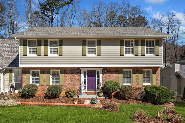 colonial inspired home with roof with shingles, brick siding, and a front lawn