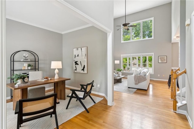 home office featuring a towering ceiling, baseboards, light wood-type flooring, and a ceiling fan