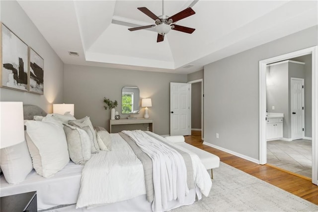 bedroom with ceiling fan, visible vents, connected bathroom, wood finished floors, and a raised ceiling