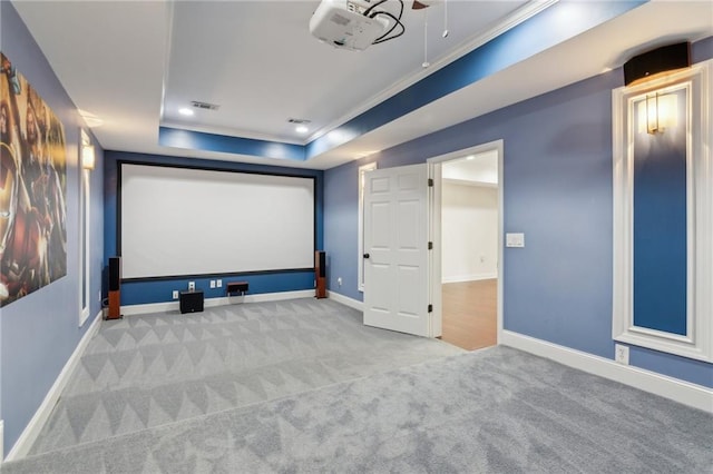 carpeted home theater featuring a tray ceiling, crown molding, visible vents, and baseboards