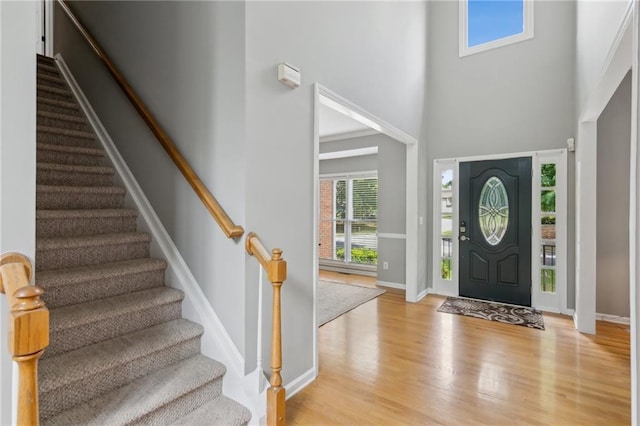 foyer entrance featuring baseboards, stairs, light wood-type flooring, and a high ceiling