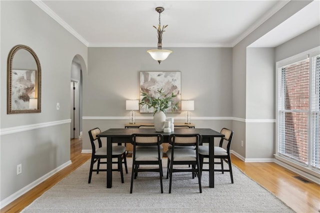 dining room featuring wood finished floors, visible vents, baseboards, arched walkways, and ornamental molding