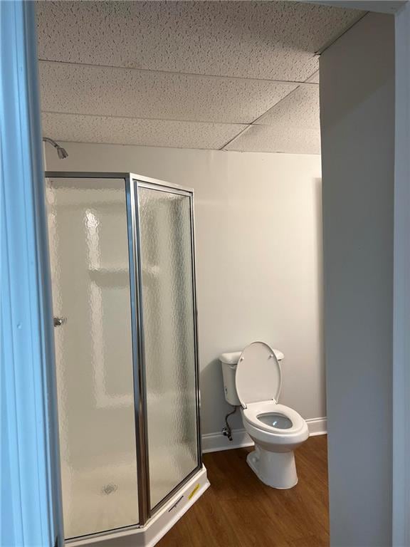 bathroom featuring a shower with door, toilet, hardwood / wood-style flooring, and a drop ceiling