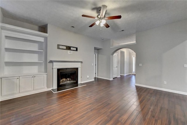 unfurnished living room with visible vents, arched walkways, a fireplace with raised hearth, dark wood-style floors, and ceiling fan