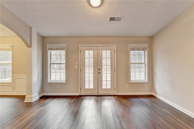 entryway with dark wood-type flooring, arched walkways, visible vents, and a textured ceiling