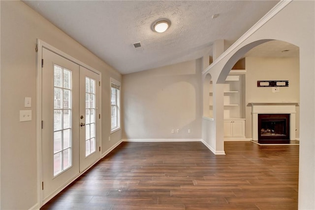 interior space featuring a textured ceiling, a fireplace, baseboards, french doors, and dark wood finished floors