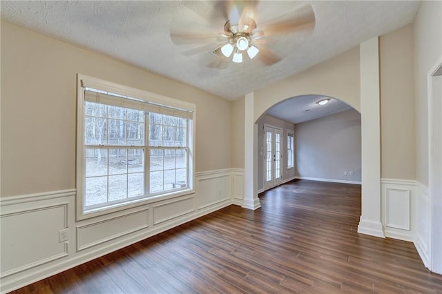 unfurnished room featuring dark wood-type flooring, arched walkways, ceiling fan, and a textured ceiling