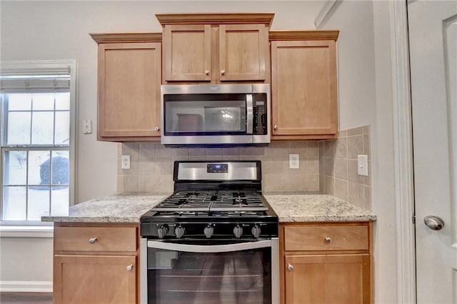 kitchen featuring range with gas stovetop, stainless steel microwave, backsplash, and light stone counters