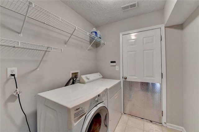 laundry area featuring light tile patterned floors, visible vents, a textured ceiling, separate washer and dryer, and laundry area