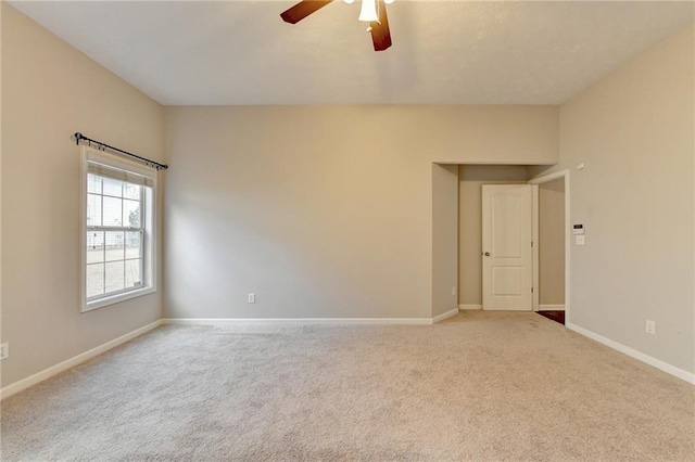 empty room featuring a ceiling fan, light colored carpet, and baseboards