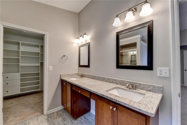 full bathroom with a walk in closet, a sink, baseboards, and double vanity