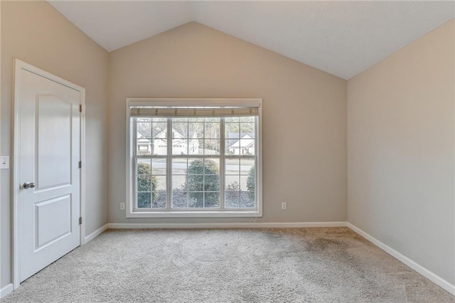 empty room featuring lofted ceiling, light colored carpet, and baseboards