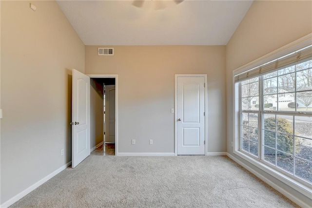 unfurnished bedroom featuring baseboards, lofted ceiling, visible vents, and light colored carpet