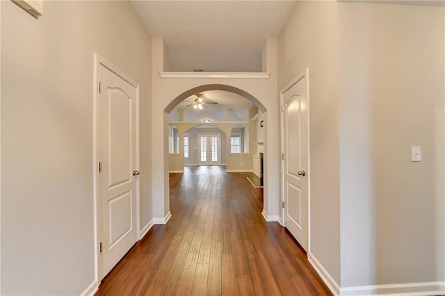 hall featuring dark wood-type flooring, arched walkways, and baseboards