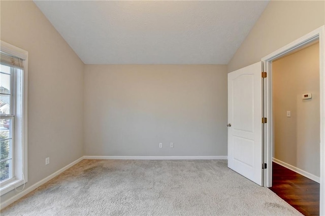 unfurnished room featuring lofted ceiling, light carpet, and baseboards