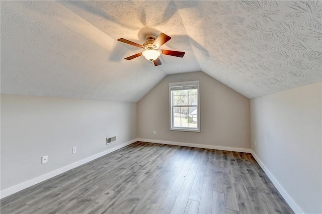 additional living space featuring baseboards, visible vents, lofted ceiling, wood finished floors, and a textured ceiling