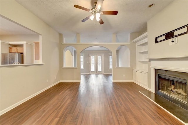 unfurnished living room featuring baseboards, arched walkways, wood finished floors, and french doors