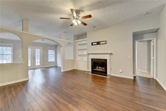 unfurnished living room featuring dark wood-style floors, baseboards, built in features, and a fireplace with raised hearth