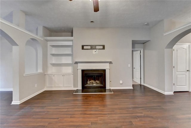 unfurnished living room featuring a fireplace with raised hearth, arched walkways, dark wood finished floors, and baseboards