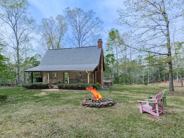 view of home's exterior featuring a chimney, log siding, a lawn, a fire pit, and roof with shingles