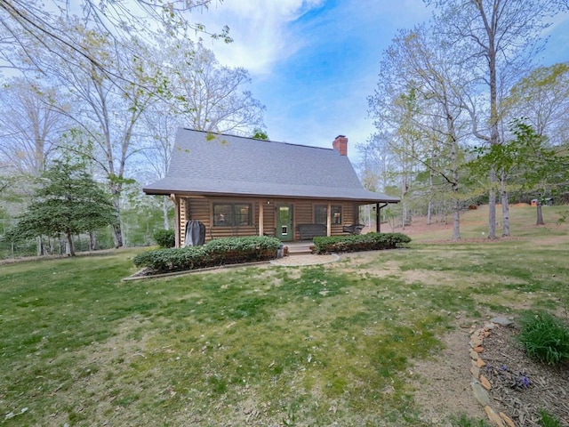 log-style house featuring a chimney, a front lawn, log siding, a porch, and roof with shingles