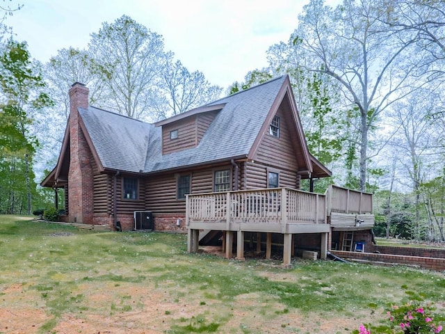 rear view of property featuring roof with shingles, a chimney, log siding, a lawn, and a deck