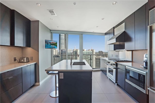 kitchen with a kitchen bar, stainless steel range, black microwave, a kitchen island with sink, and sink