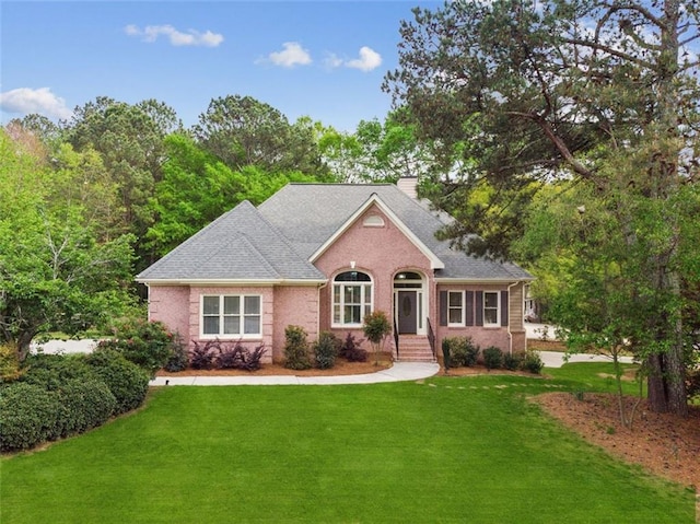 single story home featuring brick siding, a chimney, a front lawn, and roof with shingles