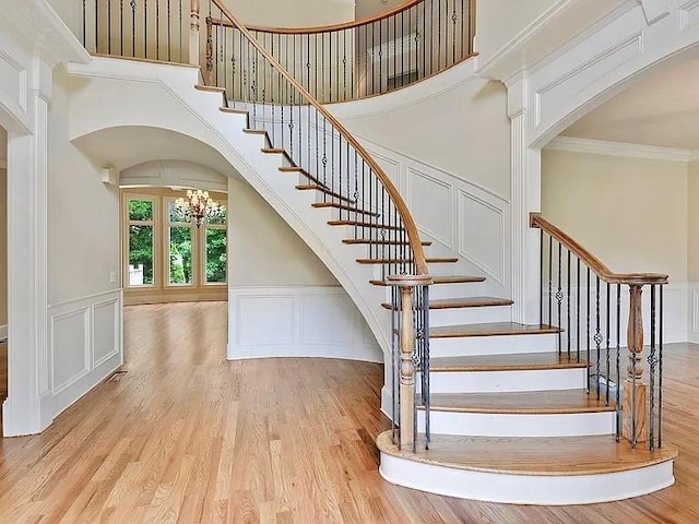 staircase featuring an inviting chandelier, ornamental molding, a decorative wall, and wood finished floors