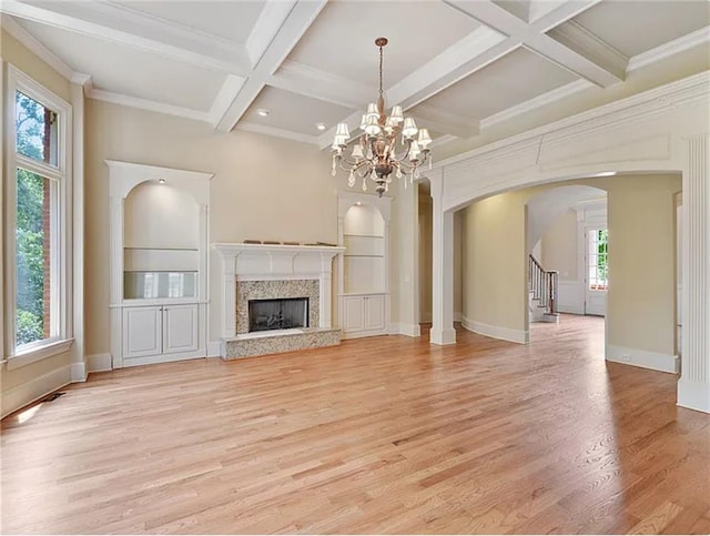 unfurnished living room with arched walkways, baseboards, a premium fireplace, stairs, and light wood-type flooring