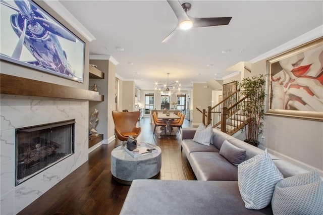 living room with a high end fireplace, ornamental molding, ceiling fan with notable chandelier, and hardwood / wood-style flooring