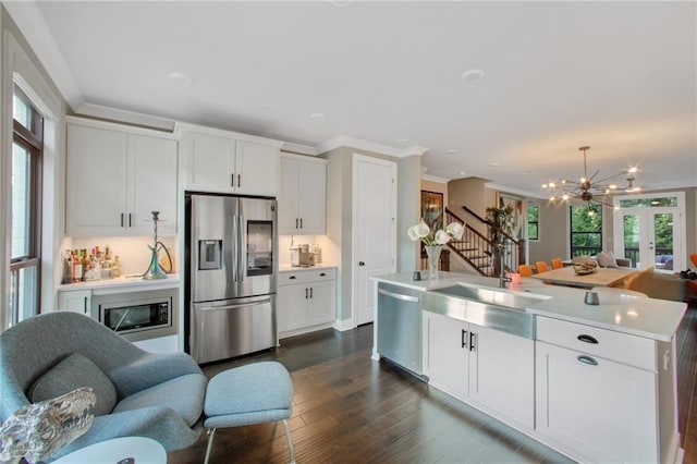 kitchen with sink, an island with sink, stainless steel appliances, ornamental molding, and white cabinets