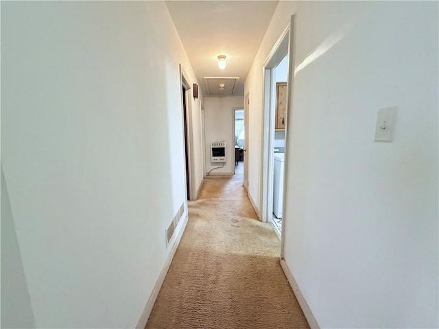 hallway featuring baseboards, heating unit, attic access, and light colored carpet