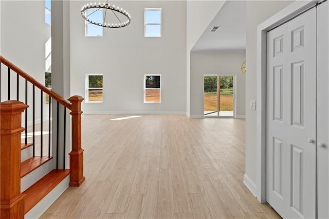 foyer with light hardwood / wood-style flooring, an inviting chandelier, and a towering ceiling