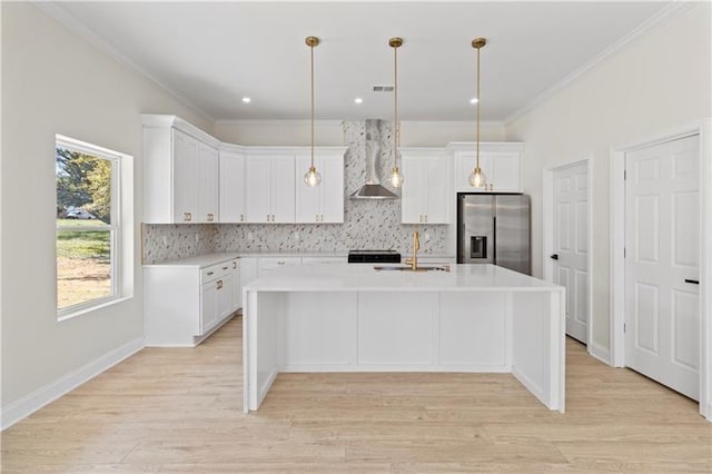 kitchen with wall chimney exhaust hood, decorative light fixtures, a center island with sink, stainless steel fridge with ice dispenser, and white cabinets